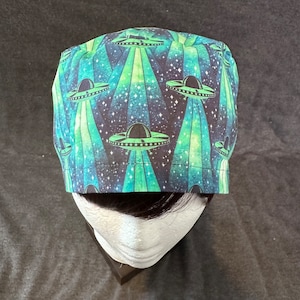May include: A blue and green patterned scrub hat with a design of flying saucers and stars.