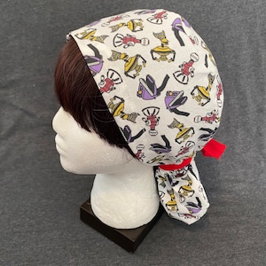 May include: A white surgical cap with a colorful pattern of robots. The cap has a red tie that is tied at the back of the head.