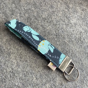 May include: A fabric key fob with a dark blue background and a repeating pattern of light blue seals and yellow stars. The key fob has a silver metal clasp and a small fabric tag.