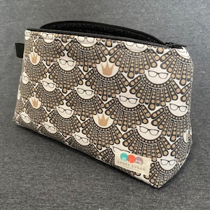 May include: A black and white zippered makeup bag with a repeating pattern of brown collars and glasses. The bag has a brown label with the text "SHORT SUGAR" in white.