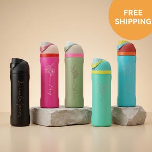 May include: Five cylindrical water bottles with flip-top lids in black, magenta, olive green, teal, and blue. Each bottle features a unique floral line art engraving and a personalised name in cursive script. The bottles are displayed on stone blocks.