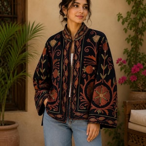 Könnte beinhalten: Schwarze Jacke mit aufwendiger Blumenstickerei in Orange-, Grün- und Goldtönen. Die Jacke hat einen Stehkragen und weite Ärmel. Das Model trägt eine blaue Jeans. Eine auffällige Jacke.