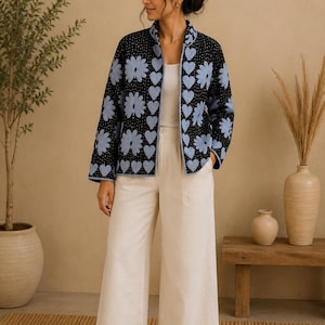 Könnte beinhalten: Schwarze Jacke mit hellblauen Blumen- und Herzmustern. Die Jacke hat einen Stehkragen und wird über einem weißen Oberteil und cremefarbenen Hosen getragen. Die Jacke ist ein gestepptes Design.