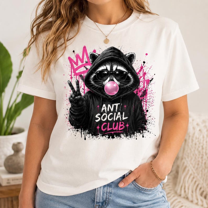 May include: White t-shirt featuring a raccoon wearing sunglasses and a black hoodie, blowing a pink bubblegum bubble. The raccoon is giving a peace sign. The words "ANTI SOCIAL CLUB" are printed on the hoodie in pink.