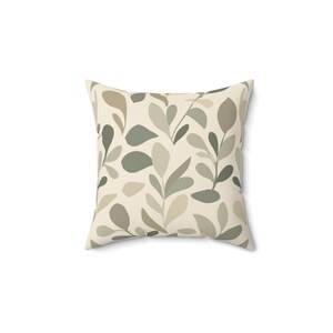 Könnte beinhalten: Ein quadratisches Dekokissen mit einem sich wiederholenden botanischen Muster aus Blättern in Salbeigrün, Olivgrün und hellem Beige auf cremefarbenem Grund. Das Design besteht aus stilisierten Stängeln und Blättern, die gleichmäßig angeordnet sind.