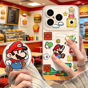 May include: A clear smartphone case featuring Super Mario graphics, including Mario, Yoshi, Toad, bricks, coins, and clouds, with a matching circular Mario phone grip. The design includes text reading World 1-1, Time 999, and Super Mario.