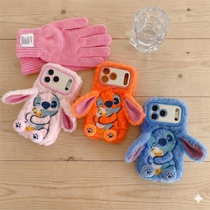 May include: Three plush phone cases in pink, orange, and blue, each with a cartoon character design. A pair of pink gloves and a clear glass container are also visible. The cases have a soft, furry texture.