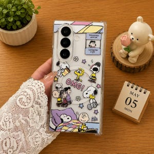 May include: A clear smartphone case featuring a Peanuts comic strip design with Snoopy, Charlie Brown, and Woodstock characters. The case includes the text "OMG!", "Psychiatric Help 5&cent;", "The Doctor Is In", and "Ah", decorated with colorful stars and flowers.