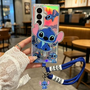 Könnte beinhalten: Eine transparente, holografische Handyhülle mit mehreren blauen Stitch-Charaktergrafiken, darunter eine große zentrale Figur, ein passender Anhänger und eine blaue Handschlaufe mit weißen Textetiketten. Die Hülle hat einen vertikalen Kameraausschnitt.