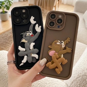 Può includere: Due custodie per telefono con i personaggi dei cartoni animati Tom e Jerry. Una custodia è nera con un design di Tom grigio, l'altra è marrone con un design di Jerry. Entrambe le custodie hanno un effetto 3D.
