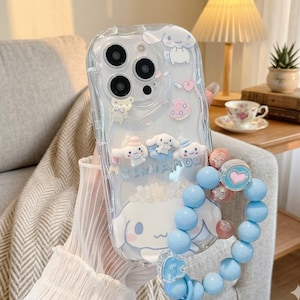 Könnte beinhalten: Transparente Handyhülle mit Cartoonfiguren und einem blauen Perlen-Handgelenkband. Die Hülle zeigt verschiedene niedliche Charaktere, Herzen und das Wort "CINNAMOROLL". Das Armband hat hellblaue Perlen und einen Herzanhänger.