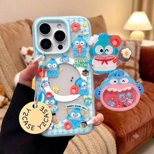 May include: A light blue and white chequered phone case featuring various blue cartoon character graphics, the text HANG YOON, and HAPPY EVERY DAY. The case includes a round beige tag labelled Y2CASE and two attached 3D character charms.