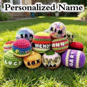 May include: A collection of round, crocheted yarn balls in various colors and patterns, each featuring a personalized name stitched in contrasting letters. The names visible include Sam, Fox, Lucy, Rox, Wendy Ann, Zac, and Gary, with the text Personalized Name.