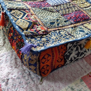 May include: A square floor cushion featuring a patchwork design of various fabrics in blue, orange, red, and gold. The surface is decorated with intricate gold embroidery, sequins, and beads. It includes small tassels and a metal zipper on the side.
