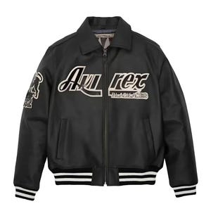 May include: A black leather bomber jacket featuring a full-length front zipper, a pointed collar, and striped ribbed cuffs and hem. The chest displays the white embroidered text "Avirex" and "BLACK ACES," with a graphic patch on the right sleeve.
