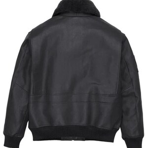 May include: A black leather bomber jacket featuring a dark gray faux fur collar, long sleeves with ribbed cuffs, and a ribbed hem. The back of the jacket displays a smooth leather finish with horizontal seam detailing across the mid-section.