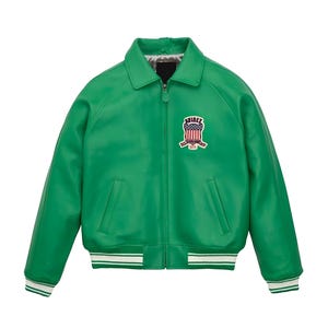 Pode incluir: Um casaco verde brilhante com fecho de correr frontal, gola pontiaguda e punhos e bainha canelados com riscas brancas. No peito esquerdo, existe um emblema com o texto Avirex e um design de escudo com a bandeira americana.