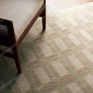May include: A beige area rug with a repeating geometric pattern of raised rectangular shapes and a textured surface, partially covered by the wooden frame and light-colored upholstered seat of a chair with a woven cane side panel.