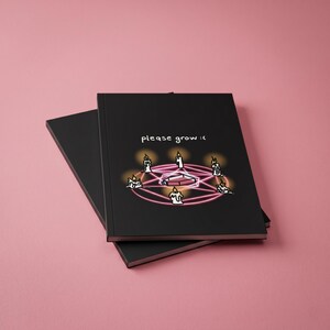 May include: Black notebook with the text "please grow :(" and a graphic of candles and a coffin inside a pink circle. The notebook is on top of another black notebook, set against a pink background.