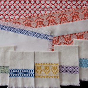 May include: A set of six white cotton tea towels with embroidered borders in various colors, including green, blue, yellow, and purple. The towels have a fringed edge.