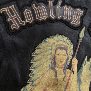 May include: Close-up of a black leather jacket with a patch displaying the word "Howling" in a vintage style. Below, a Native American woman with a feathered headdress and spear is shown. The jacket has a textured surface.