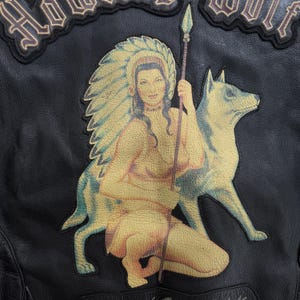May include: Black leather jacket with a large patch depicting a Native American woman and a wolf. The woman wears a headdress and holds a spear. The words "HOWL WOLF" are embroidered above the patch.