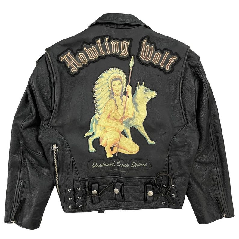 May include: Black leather jacket with a "Howling Wolf" design on the back. The design features a Native American woman, a wolf, and the text "Deadwood, South Dakota". The jacket has a classic biker style with zippers and a button closure.