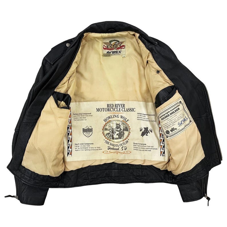 May include: Black leather motorcycle jacket with a cream lining. The lining displays printed graphics and text, including "Red River Motorcycle Classic" and "Howling Wolf." The jacket has multiple pockets and a zip closure.