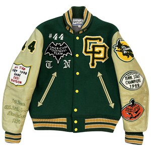 以下が含まれることがあります： 緑とクリーム色のスタジアムジャンパー。複数のワッペン付き。「#44」、「American Football Team」、「T」、「N」、「All Star 1989 1990 Game East Division」、「Tenn. State Champions 1989」、「Div. Champ 89」など。襟、袖口、ウエストバンドにストライプが入っています。