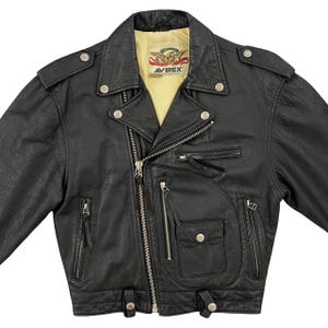 May include: Black leather motorcycle jacket with multiple zipped pockets, snap fastenings, and a notched collar. The jacket features the brand name "AVIREX" on a patch inside the collar. The jacket has a classic biker style.