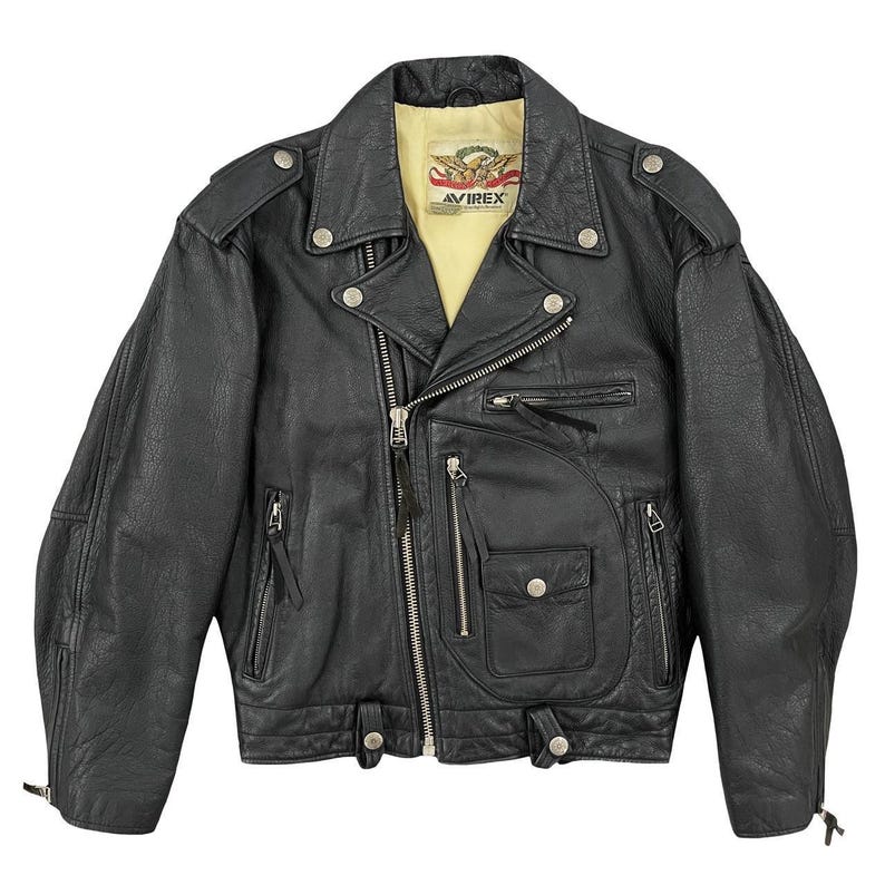 May include: Black leather biker jacket with a notched collar, multiple zipped pockets, and snap fastenings. The jacket has a yellow lining and the "AVIREX" logo. The jacket has a classic biker style.