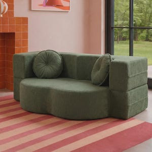May include: A sage green loveseat with a textured, nubby fabric finish. The sofa features a curved, kidney-bean-shaped seat base, blocky armrests, and two matching round, tufted throw pillows placed against the backrest cushions.