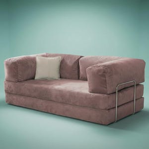 May include: A mauve corduroy sofa featuring a low-profile design with thick, rectangular armrests and a matching backrest. A single square off-white throw pillow rests on the seat. The sofa is supported by a thin, silver-toned metal frame.