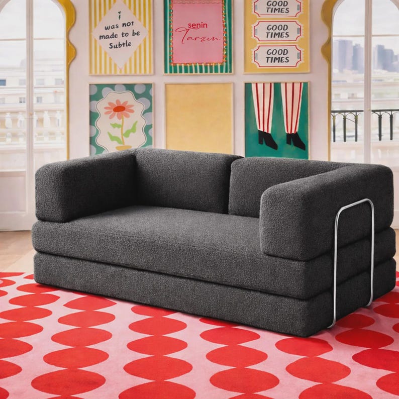 May include: A dark gray sofa with a textured, nubby fabric finish and a low-profile design. The sofa features a rectangular frame with rounded corners and a silver-toned metal support structure on the side, providing a clean and structured appearance.
