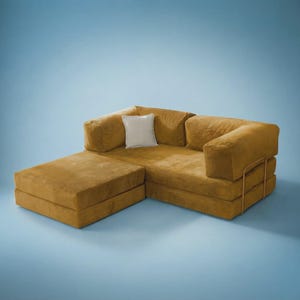 May include: A mustard yellow modular sofa with a low-profile design, featuring a rectangular chaise section, thick cushioned backrests, and a single square off-white throw pillow. The sofa is supported by a thin, gold-toned metal frame structure.