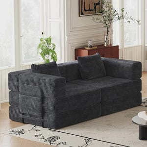 May include: A dark gray corduroy sofa featuring a modular design with thick, rectangular armrests and two matching square throw pillows. The fabric has a distinct vertical ribbed texture, and the structure consists of two main seating sections.