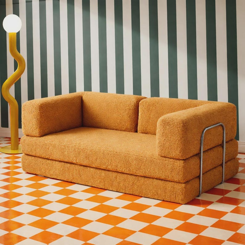 May include: A mustard yellow, textured, multi-layered sofa with a low back and armrests, featuring a silver metal frame on the side. Beside the sofa stands a tall, yellow, wavy floor lamp with a spherical white light bulb at the top.