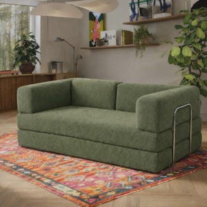 May include: A sage green sofa with a textured, boucl&eacute;-style fabric upholstery. The sofa features a low-profile, blocky design with a single continuous seat cushion, a backrest, and two armrests, accented by a polished chrome metal frame support.