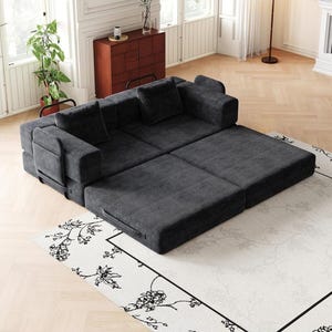 May include: A dark gray modular sofa bed upholstered in corduroy fabric. The piece features a low-profile design with two back cushions and two side armrests, configured in a partially extended position to create a flat sleeping surface area.