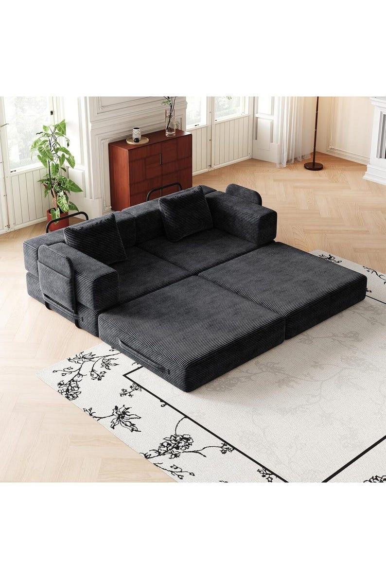 May include: A dark gray modular sofa bed upholstered in corduroy fabric. The piece features a low-profile design with two back cushions and two side armrests, configured in a partially extended position to create a flat sleeping surface area.