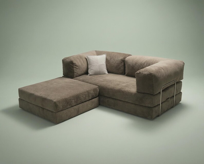 May include: A brown modular sofa with a low-profile design, featuring a rectangular ottoman section, thick cushioned seating, and a single light-colored square throw pillow. The sofa is supported by a thin, metallic frame visible on the side.