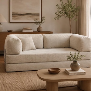 May include: A cream-colored corduroy sofa with a low-profile design, featuring thick, rounded armrests and a matching square throw pillow. The upholstery has a distinct vertical ribbed texture, and the sofa is positioned on a woven rug.