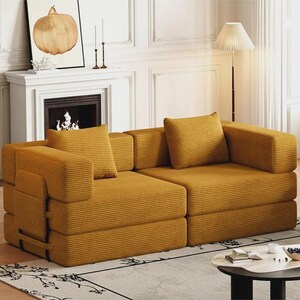 May include: A mustard yellow corduroy sofa featuring a modular design with two distinct sections, thick square armrests, and two matching square throw pillows. The fabric has a prominent horizontal ribbed texture across the entire surface.