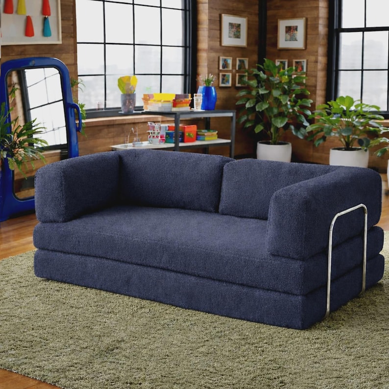 May include: A dark blue, textured fabric sofa featuring a low-profile design with a thick, multi-layered seat and backrest. The sofa is supported by a sleek, U-shaped silver metal frame that wraps around the exterior of the armrests.