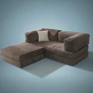 May include: A brown modular sofa with a low-profile design, featuring a chaise lounge section, thick cushioned armrests, and a single square off-white throw pillow. The sofa is supported by a thin, visible metal frame structure on the side.