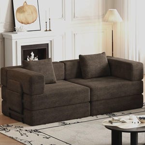 May include: A dark brown corduroy sofa featuring a low-profile design with two distinct seating sections, thick square armrests, and two matching square throw pillows. The fabric has a prominent vertical ribbed texture throughout the entire piece.
