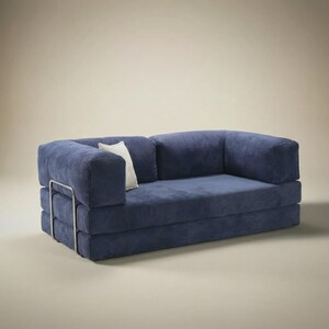 May include: A navy blue corduroy sofa featuring a low-profile design with thick, blocky cushions and a metallic silver frame visible on the side. A single small, off-white rectangular throw pillow is tucked against the left armrest.
