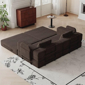 May include: A dark brown modular sofa bed with a textured corduroy fabric finish. The piece features a low-profile design with multiple square back cushions and a wide, flat base that extends outward to create a large, level sleeping surface.