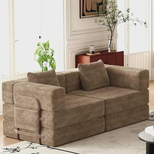 May include: A modular sofa upholstered in brown corduroy fabric, featuring a low-profile design with two square back cushions and a side panel attached with straps. The sofa consists of two distinct sections joined together to form a loveseat.