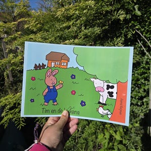Könnte beinhalten: Ein rechteckiges Kinderbuchcover mit einem gezeichneten Hasen in blauer Latzhose, der ein gelbes Küken hält, einer schwarz-weißen Kuh, einem kleinen Haus und Blumen auf einer grünen Wiese. Der Text lautet Tim en de kuikens und Astrid Reijman.